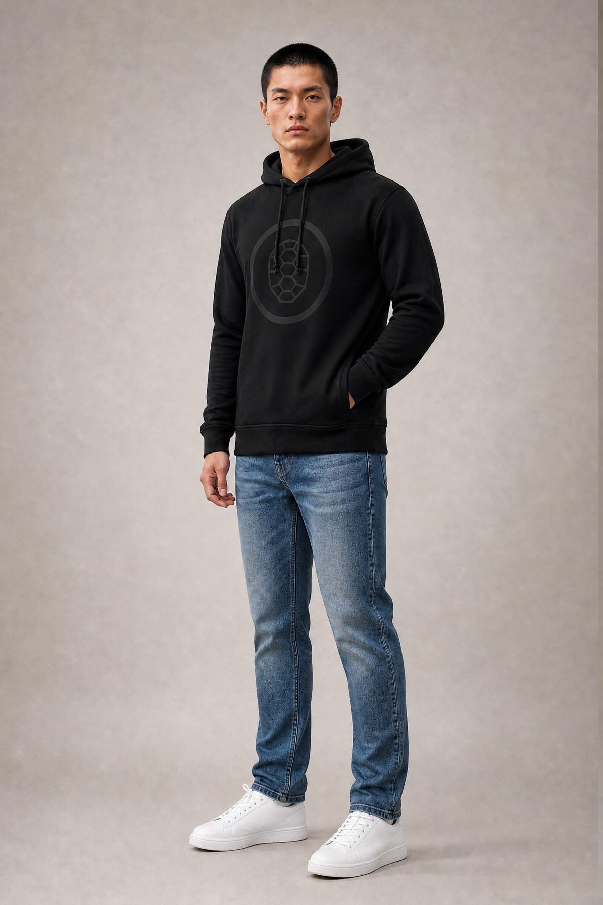 Jun wearing the black ONETURTLE hoodie with tonal turtle logo and blue jeans, full-body studio photo for the hoodies category
